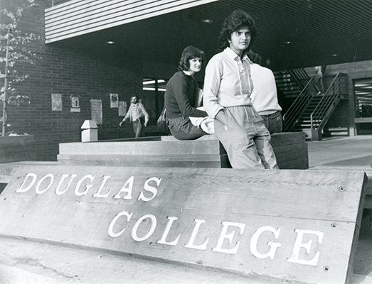 Students sitting beside a wooden Douglas College sign